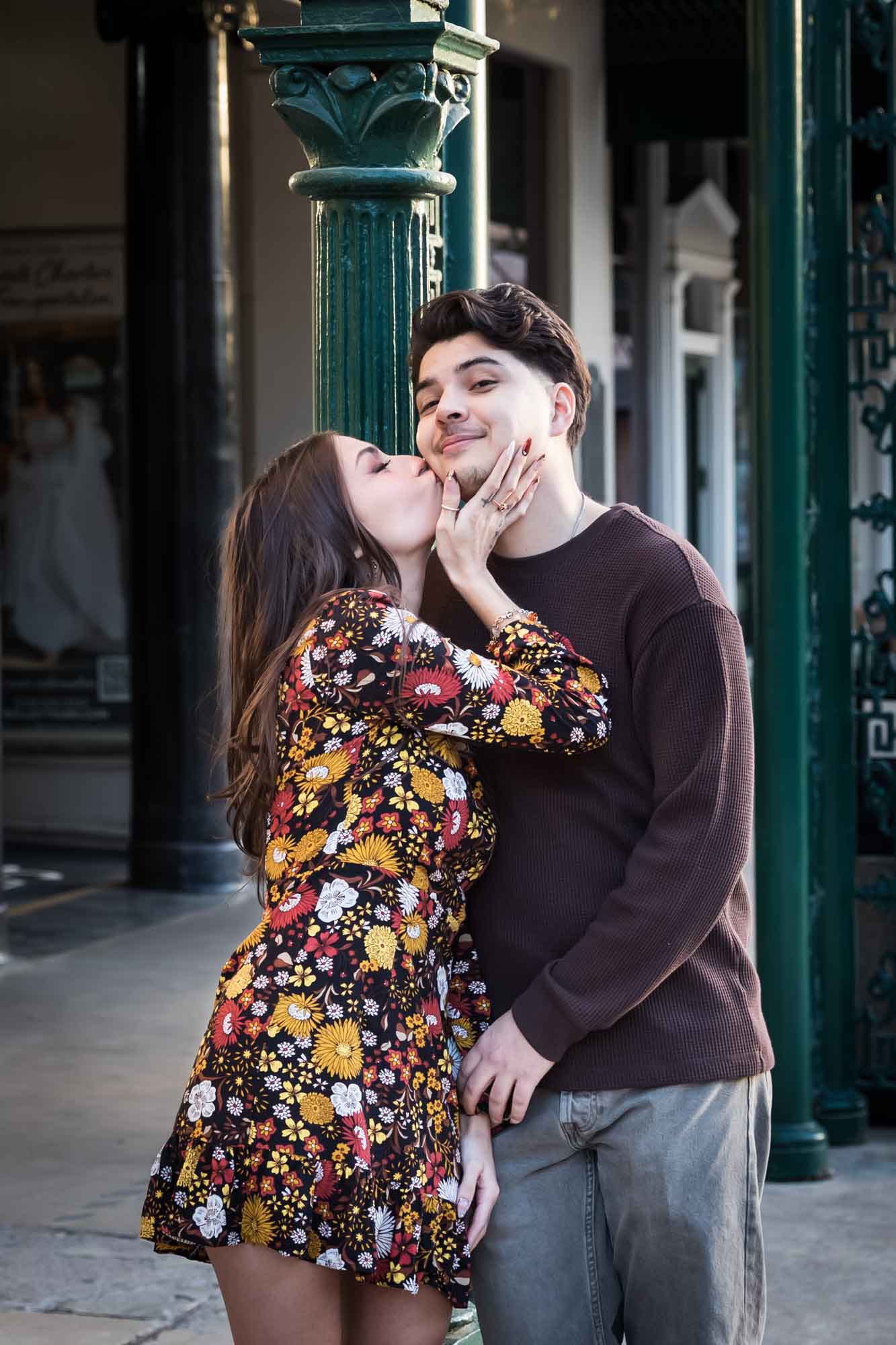 Woman kissing man in front of green column of Menger Hotel during a downtown San Antonio surprise proposal
