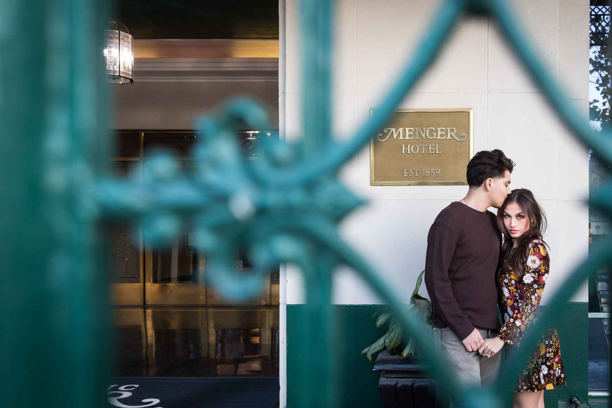 View of couple hugging through green wrought iron gate of Menger Hotel during a downtown San Antonio surprise proposal