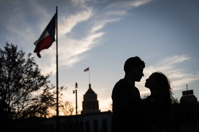 Silhouette photo of man and woman against San Antonio skyline with Texas flag waving during a downtown San Antonio surprise proposal
