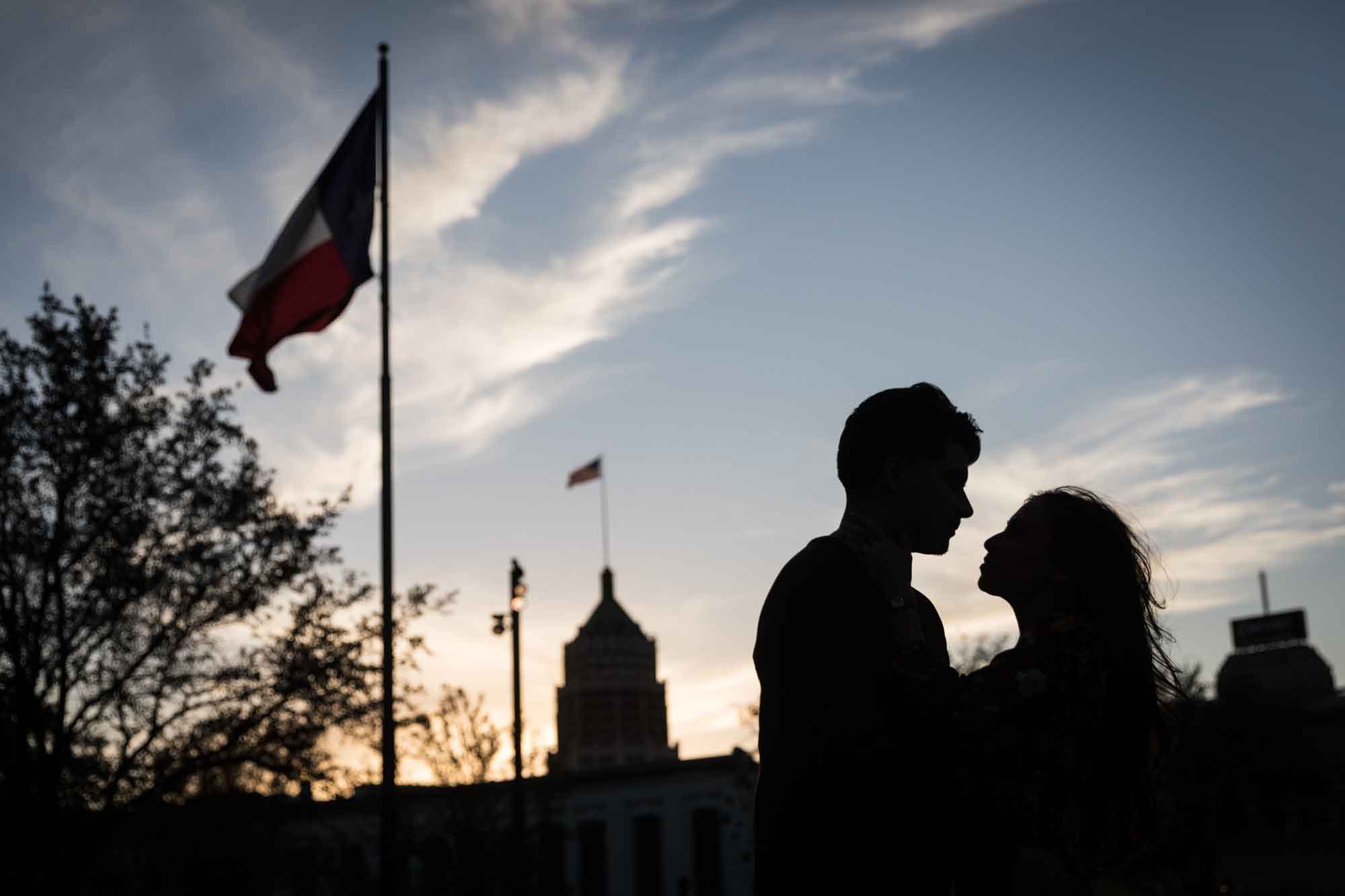 Silhouette photo of man and woman against San Antonio skyline with Texas flag waving during a downtown San Antonio surprise proposal