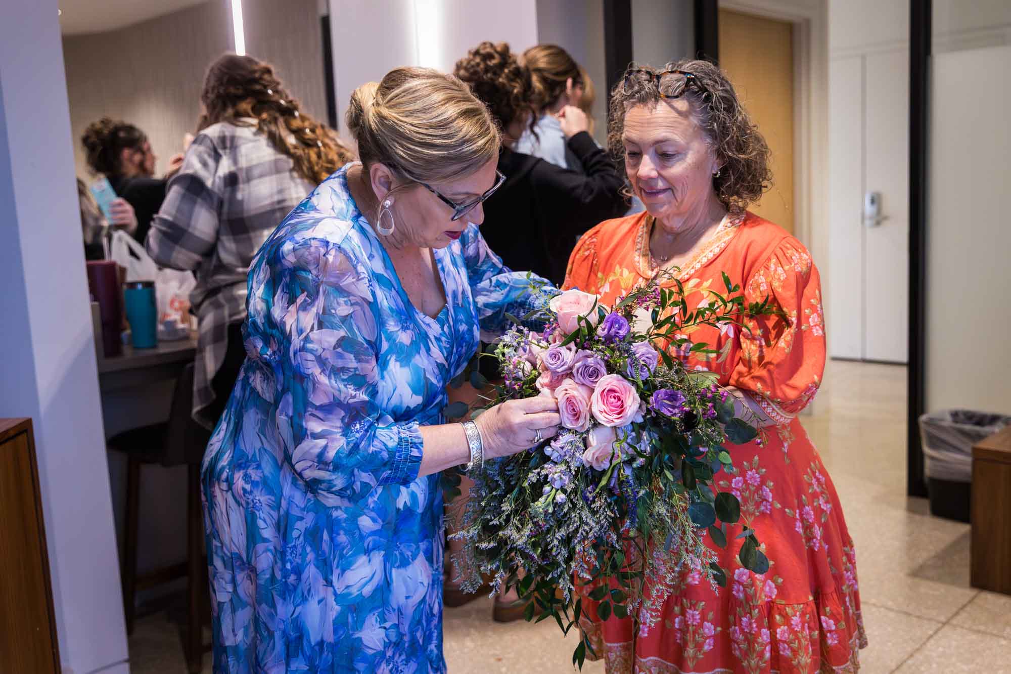 Two older woman fixing a flower bouquet filled with pink and purple roses before a San Antonio Botanical Garden wedding ceremony