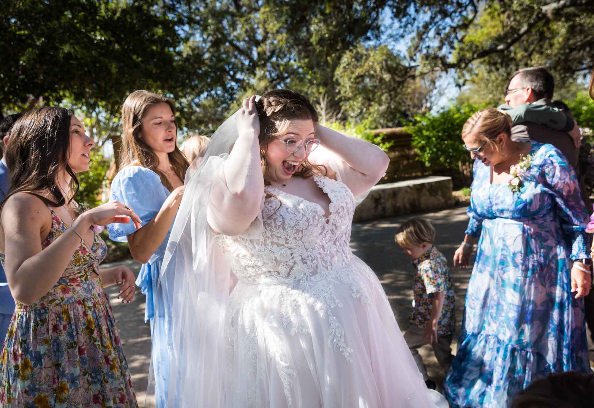 Female guests helping bride put back in veil outdoors after a San Antonio Botanical Garden wedding ceremony