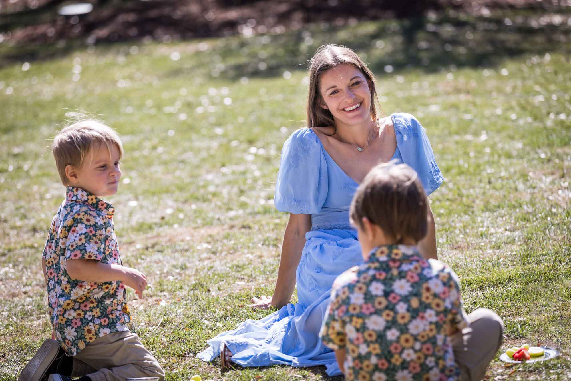 Woman wearing blue dress sitting on lawn with two little boys after a San Antonio Botanical Garden wedding ceremony