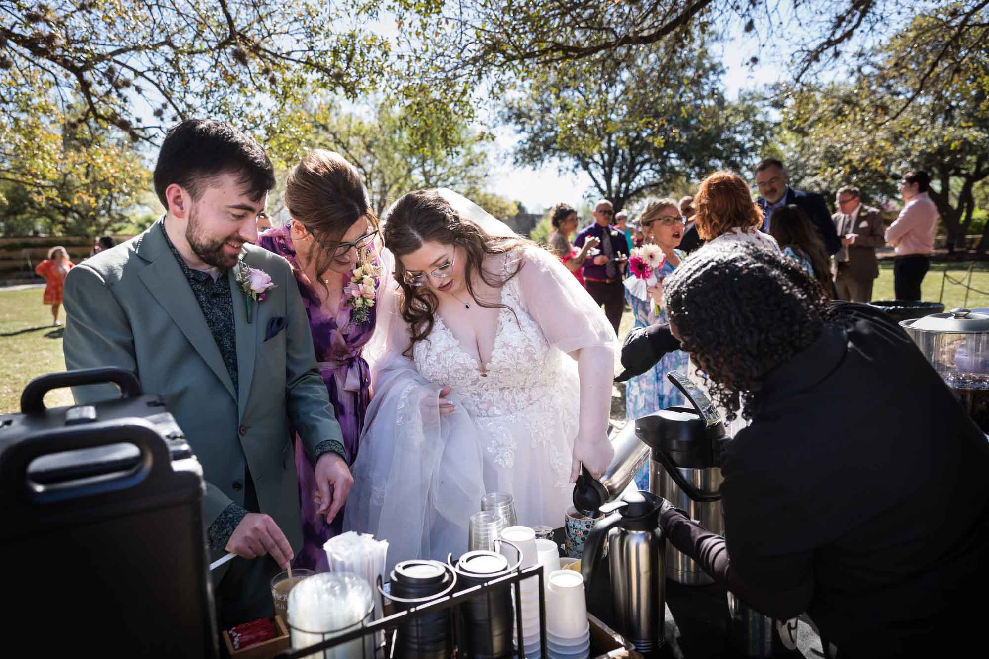 Bride and groom standing with woman pouring coffee after a San Antonio Botanical Garden wedding ceremony
