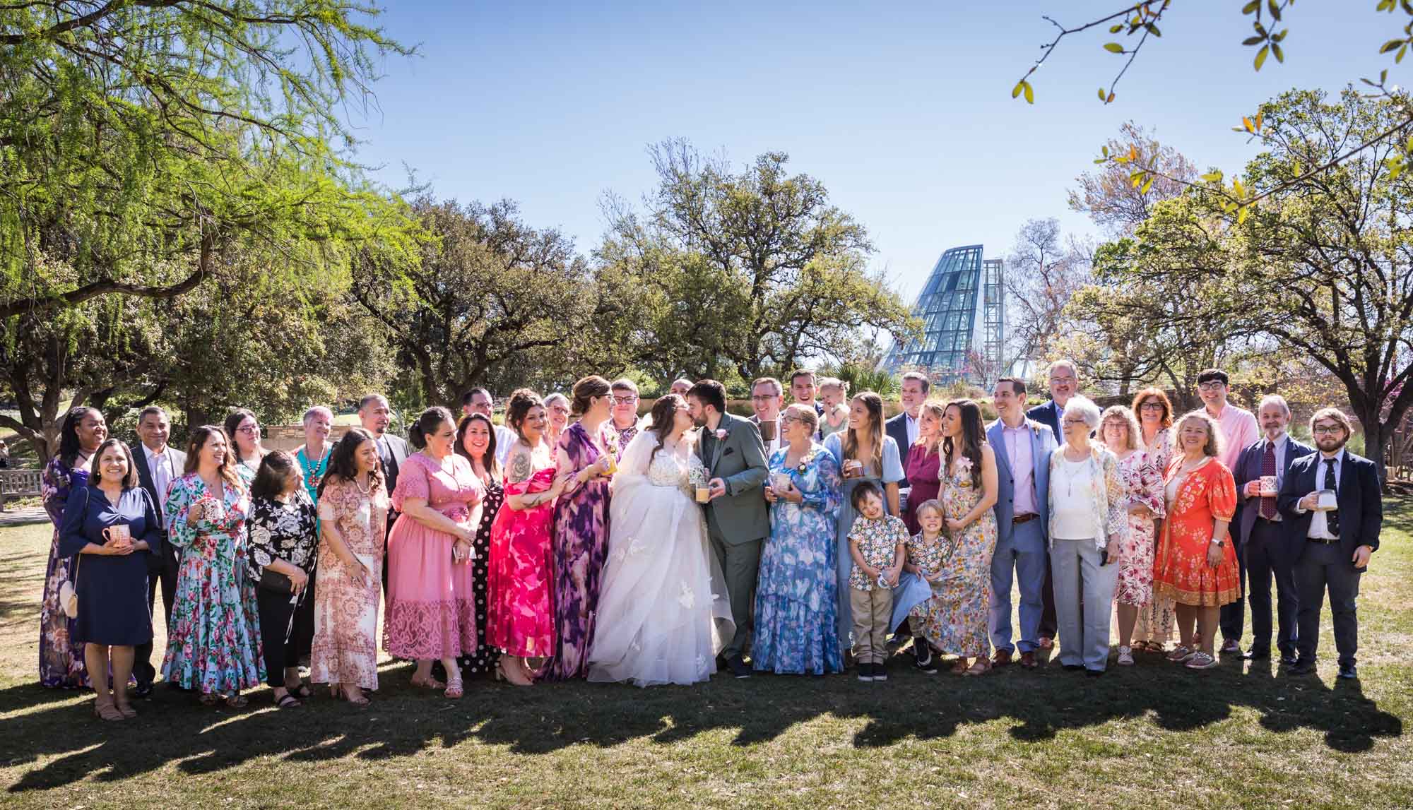 All guests cheering for bride and groom who are kissing on lawn after a San Antonio Botanical Garden wedding ceremony