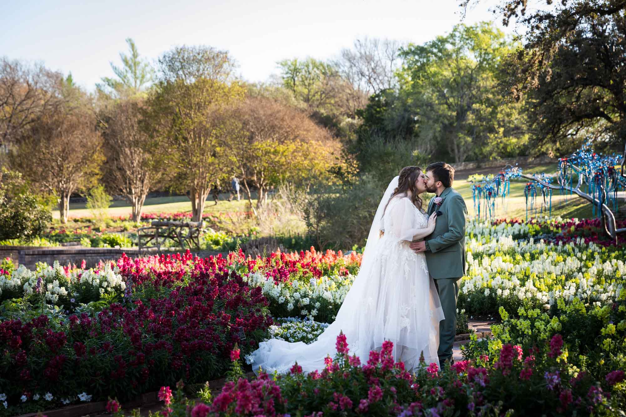 Bride and groom kissing in front of bed of colorful snapdragons and trees before a San Antonio Botanical Garden wedding ceremony