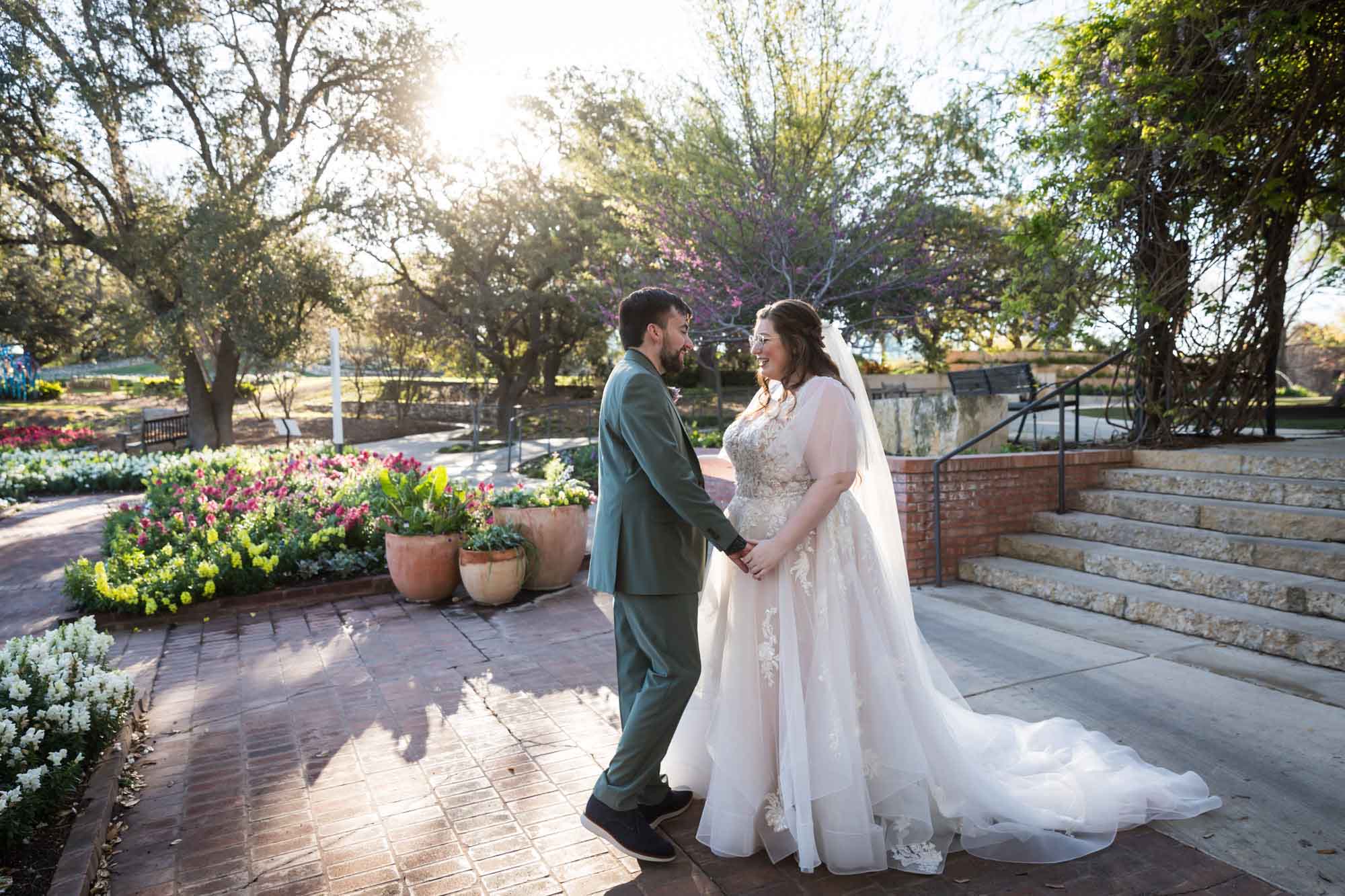 Bride and groom holding hands in front of flowers and stone stairs before a San Antonio Botanical Garden wedding ceremony