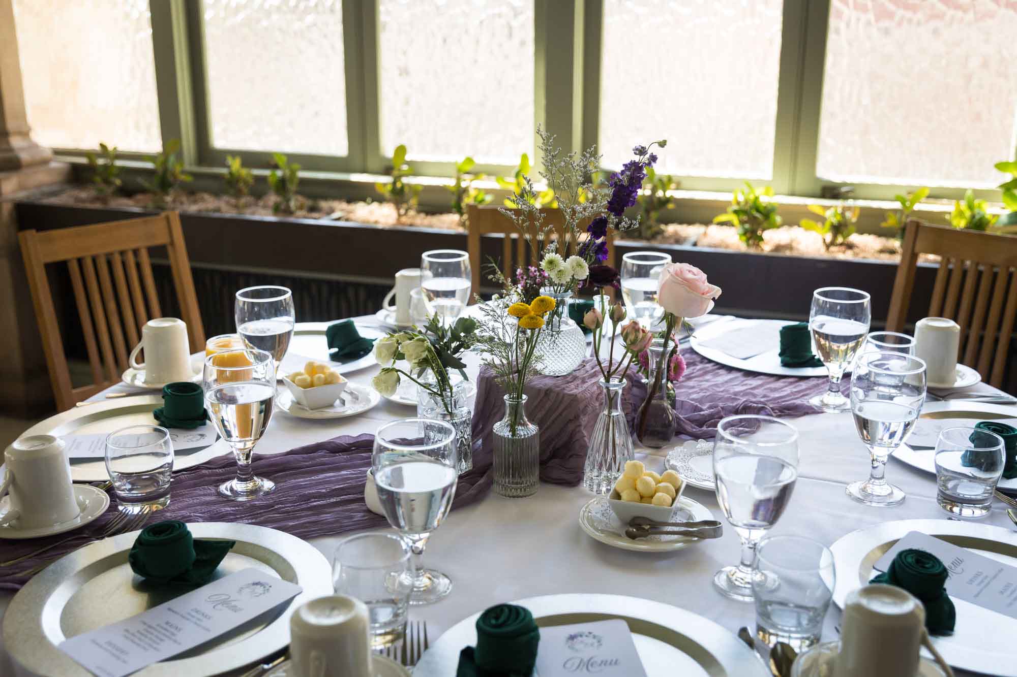 Table set with several vases filled with colorful flowers in front of a window during a Guenther House wedding reception