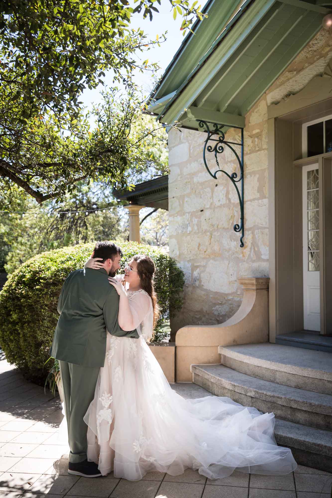 Bride and groom hugging in front of stairs, bush, and door during a Guenther House wedding reception