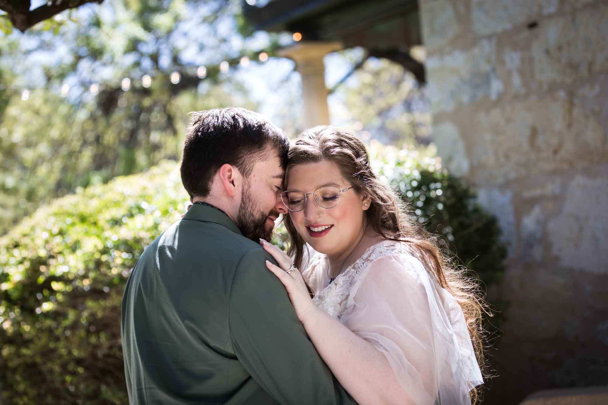 Bride and groom hugging in front of bush and stone wall during a Guenther House wedding reception