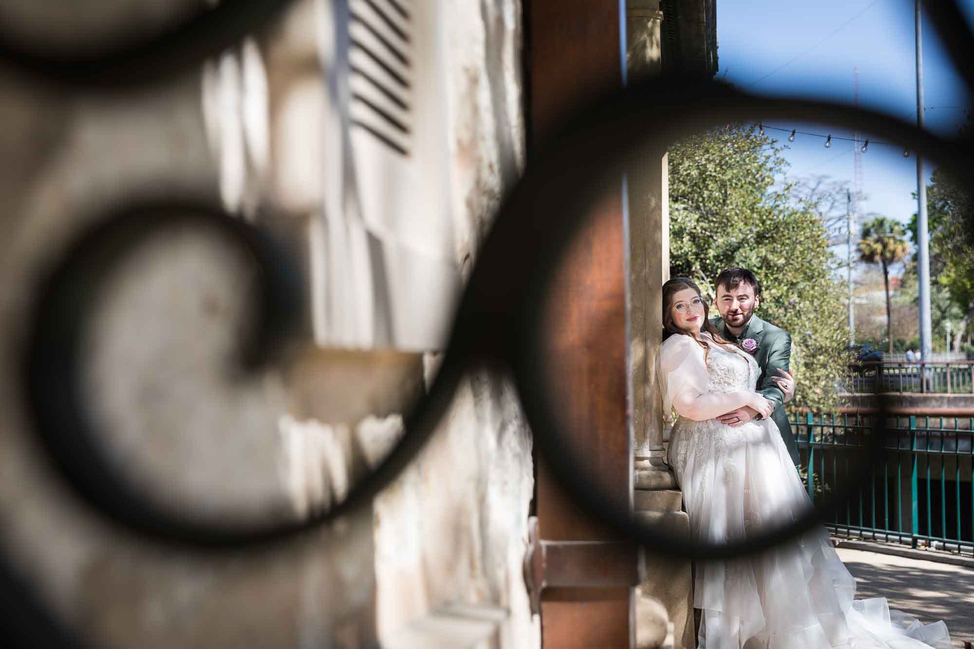Bride and groom leaning against column as seen through metal railing during a Guenther House wedding reception