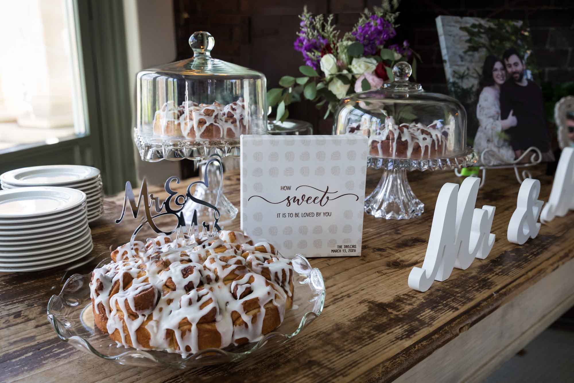 Wooden table set with clear cake stands holding cinnamon buns during a Guenther House wedding reception