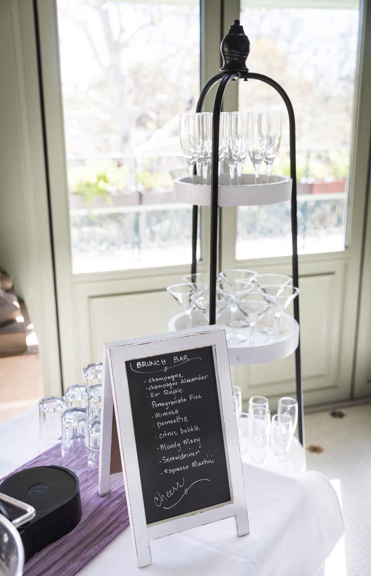 Beverage bar with chalkboard sign showing drinks available and tiered stand holding glasses during a Guenther House wedding reception