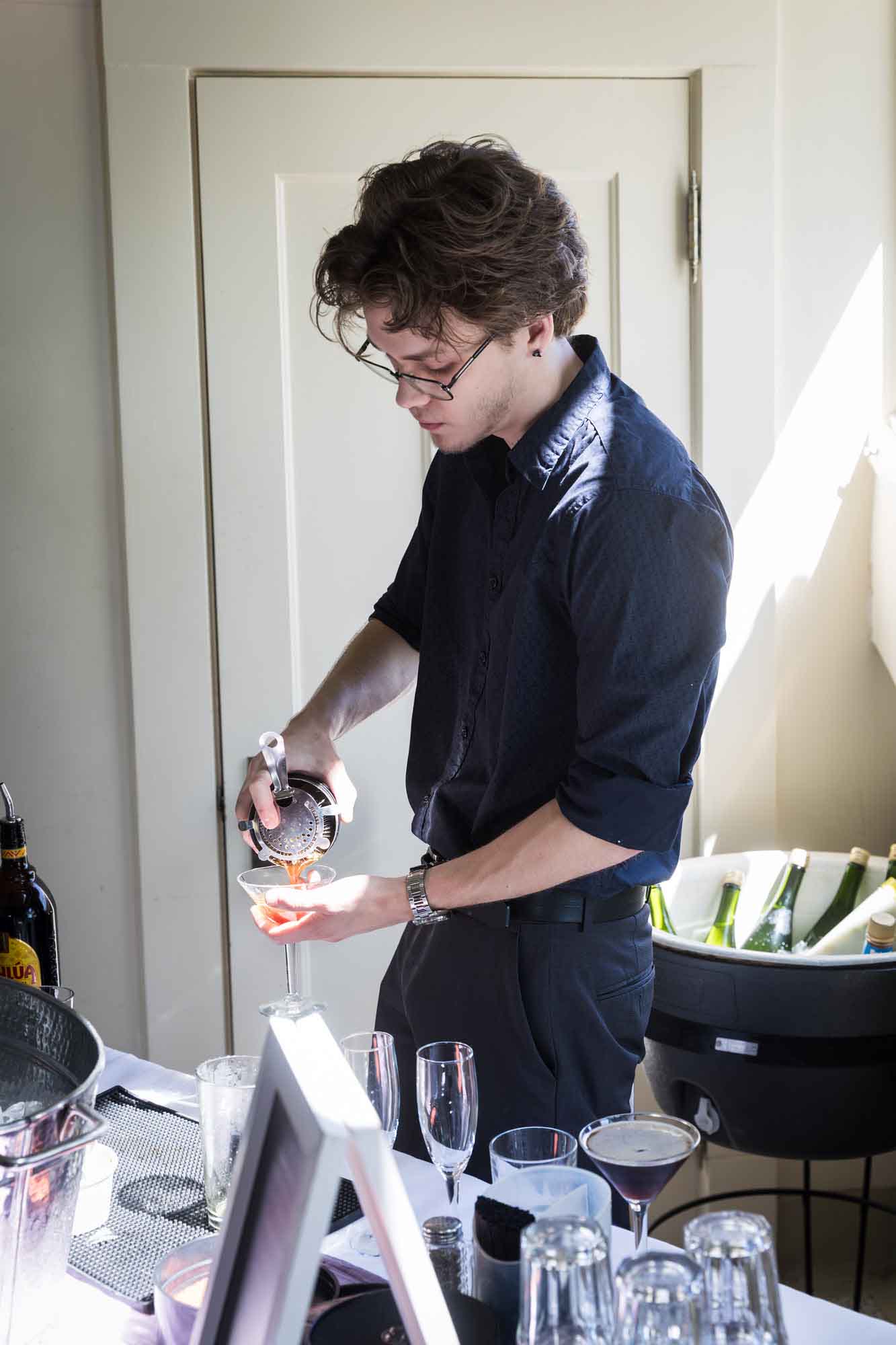 Bartender pouring drink from martini shaker into martini glass at bar during a Guenther House wedding reception
