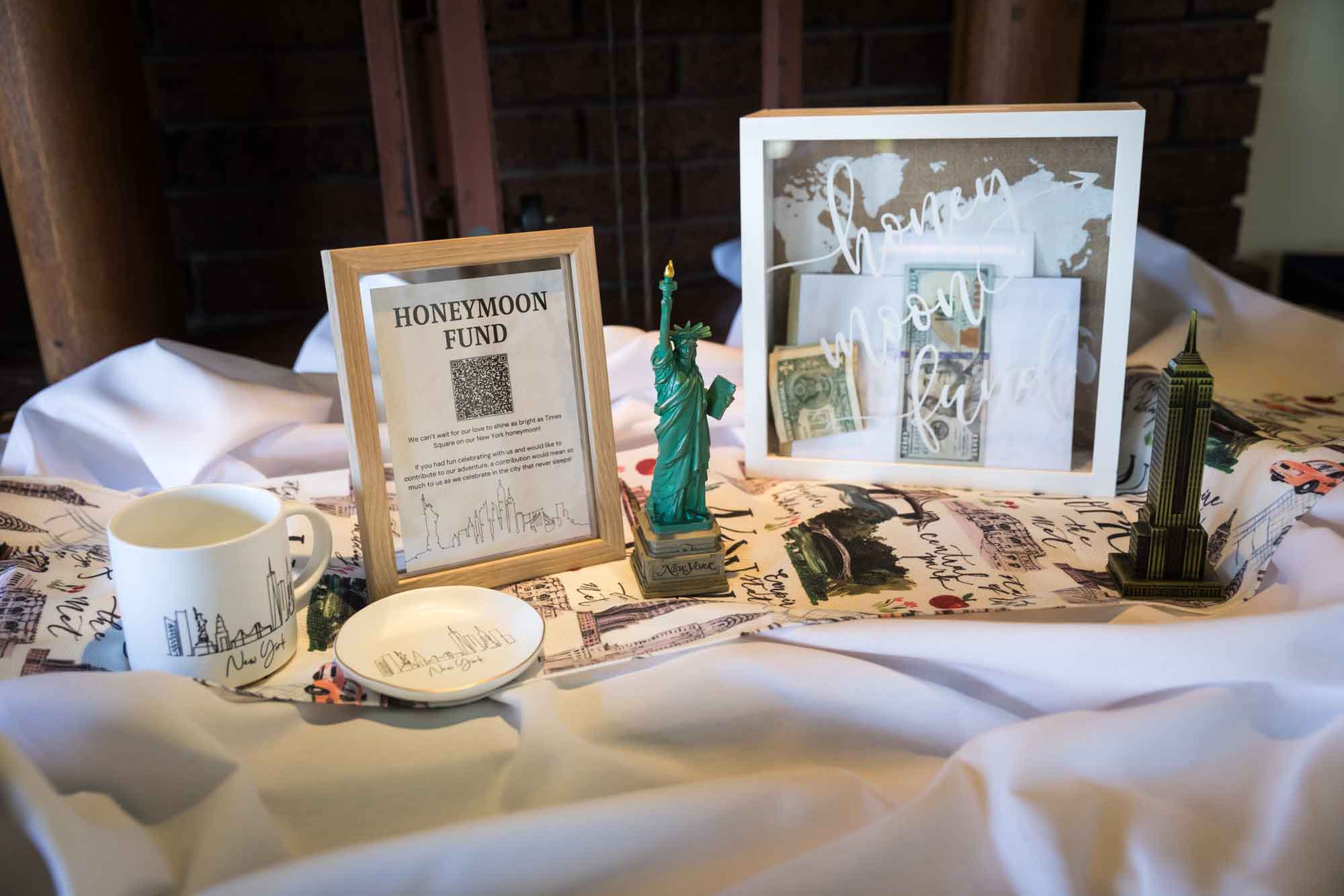 Table showing honeymoon fund sign, small Empire State Building statue, and Statue of Liberty statue on table during a Guenther House wedding reception