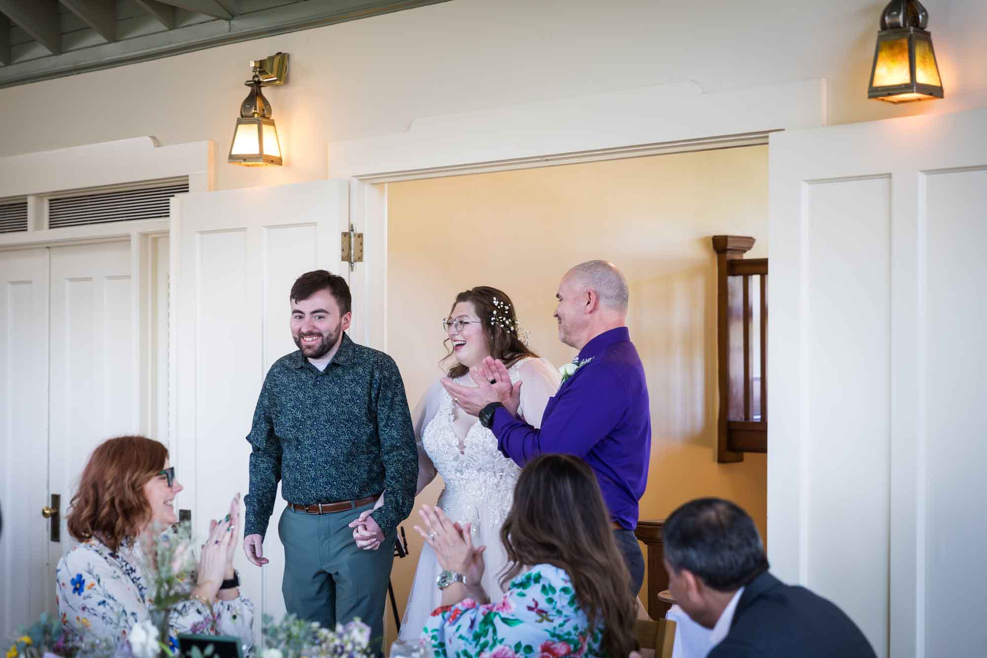 Guests clapping as bride and groom enter room holding hands during a Guenther House wedding reception