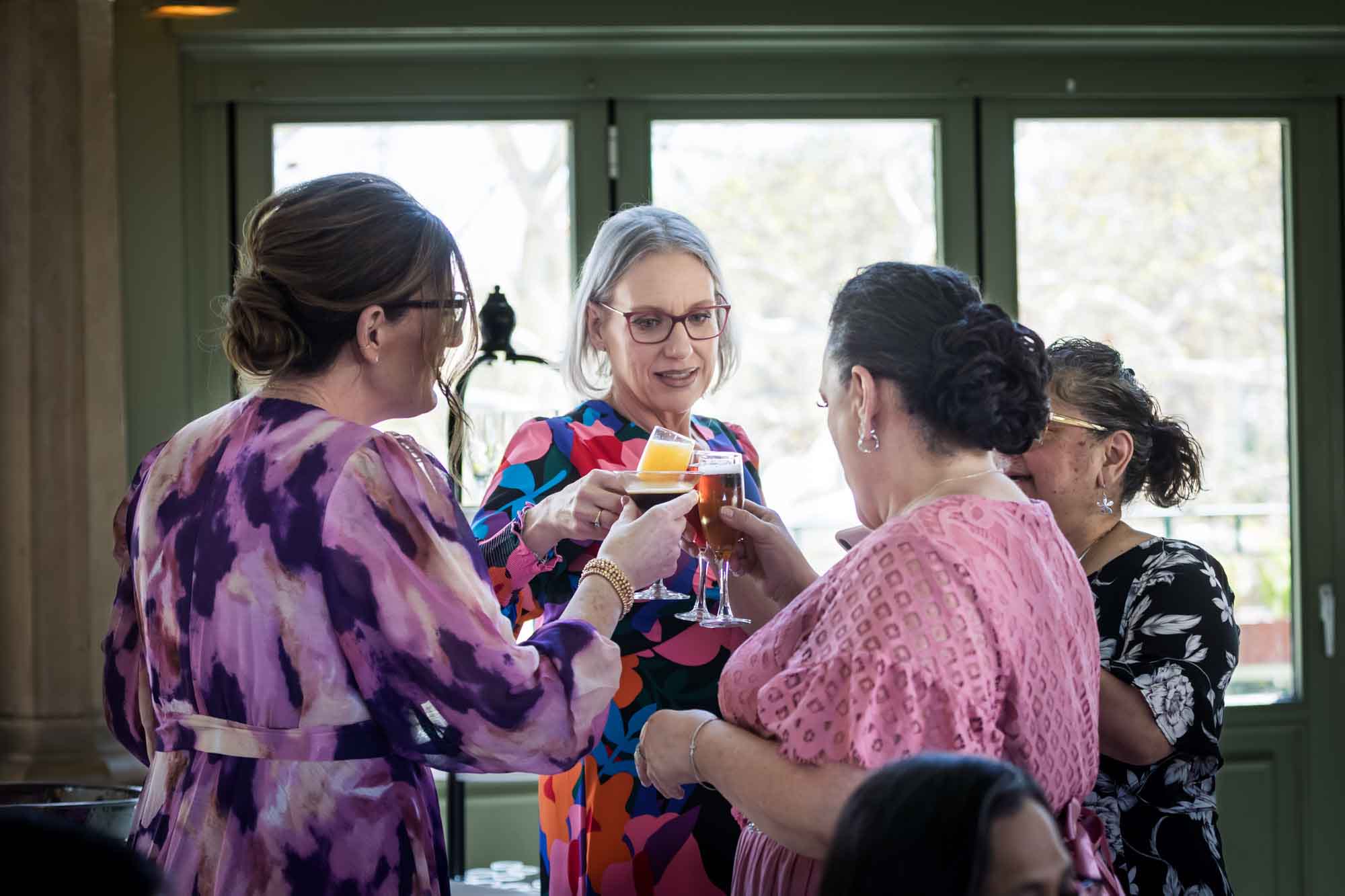 Four female guests cheering with glasses in front of window during a Guenther House wedding reception
