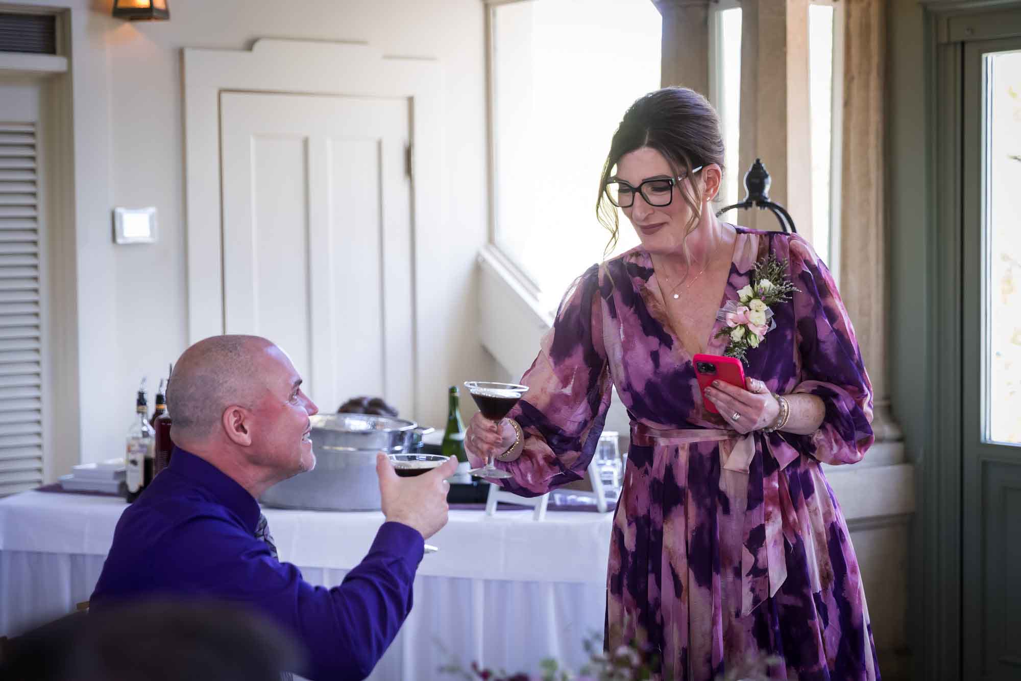 Woman wearing purple floral dress cheering espresso martini with man during a Guenther House wedding reception