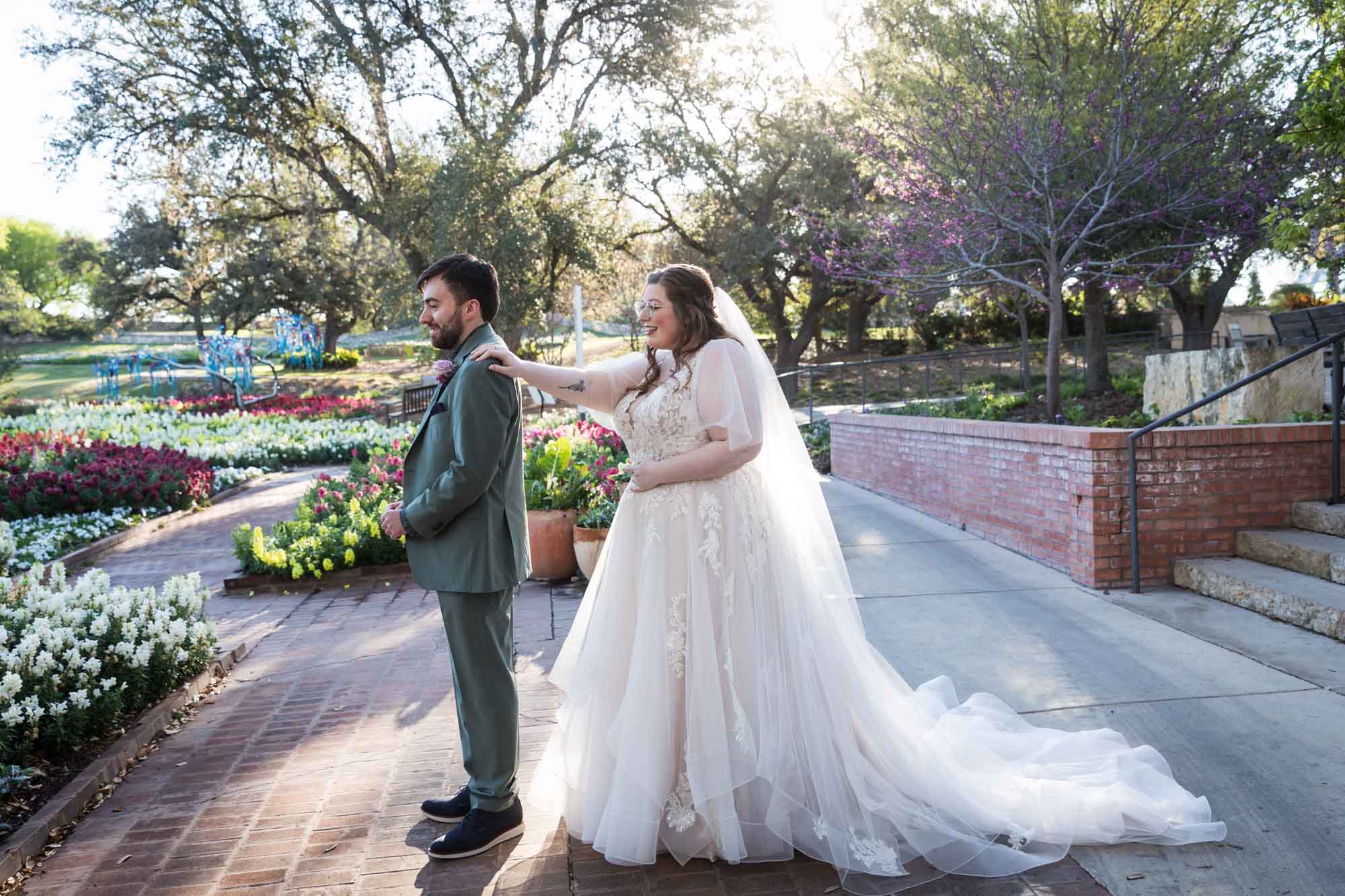 Bride wearing white dress and veil tapping groom on shoulder during first look before a San Antonio Botanical Garden wedding ceremony