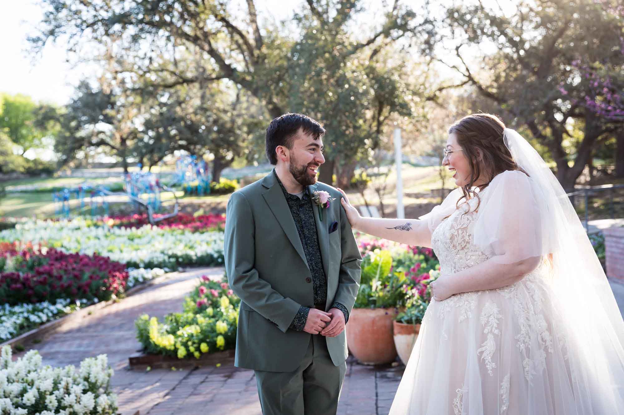 Bride wearing white dress and veil with hand on groom's shoulder during first look before a San Antonio Botanical Garden wedding ceremony