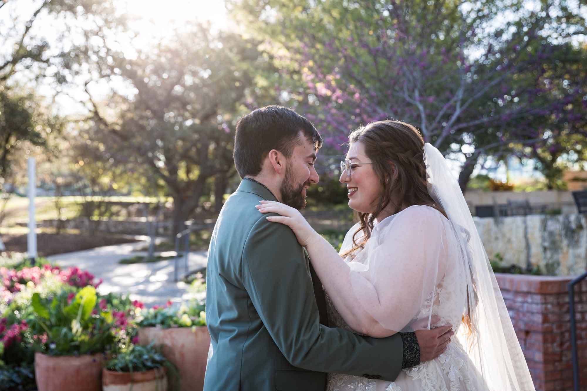 Bride and groom hugging in front of flower gardens during first look before a San Antonio Botanical Garden wedding ceremony
