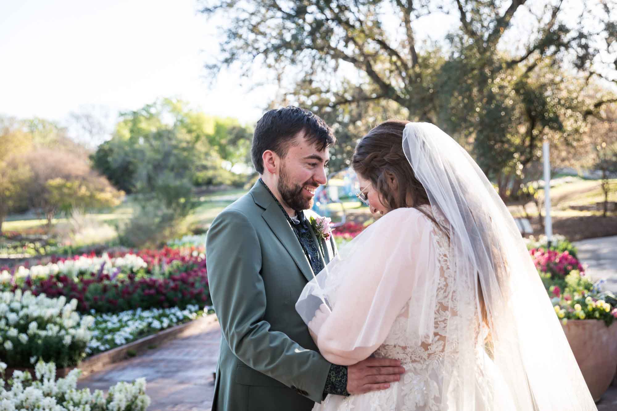 Groom looking at bride wearing white dress and veil during first look in front of flower gardens before a San Antonio Botanical Garden wedding ceremony