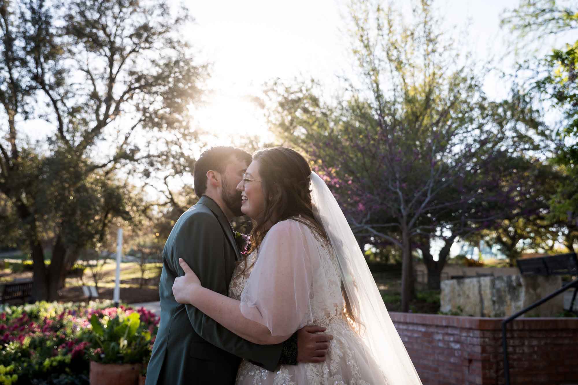 Bride and groom hugging in front of flowers and trees during first look before a San Antonio Botanical Garden wedding ceremony