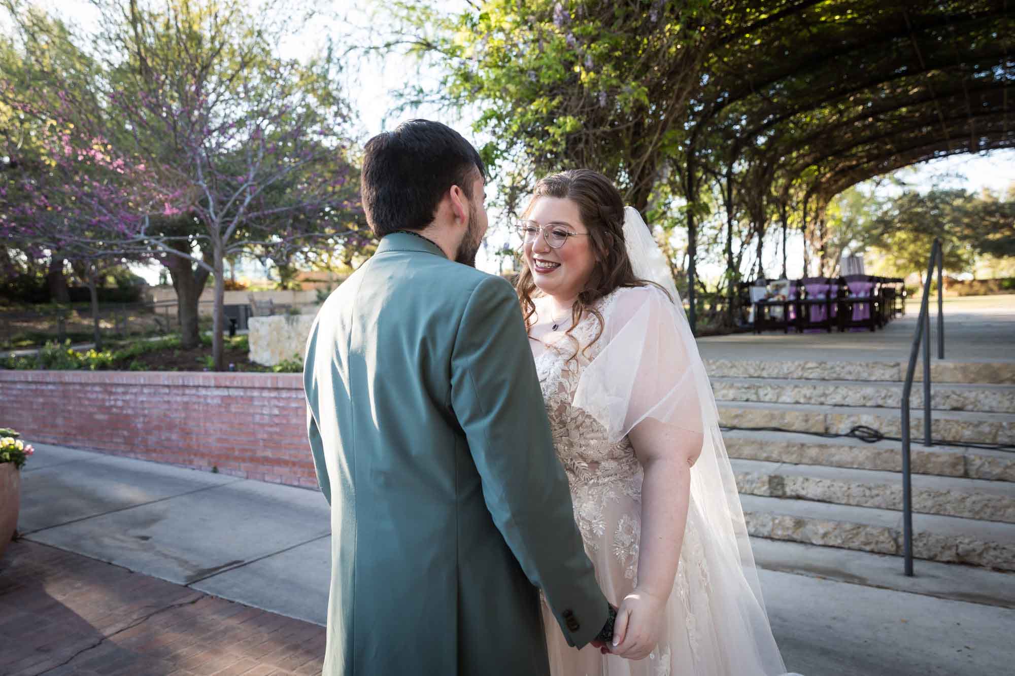 Bride and groom holding hands in front of stairs during first look before a San Antonio Botanical Garden wedding ceremony