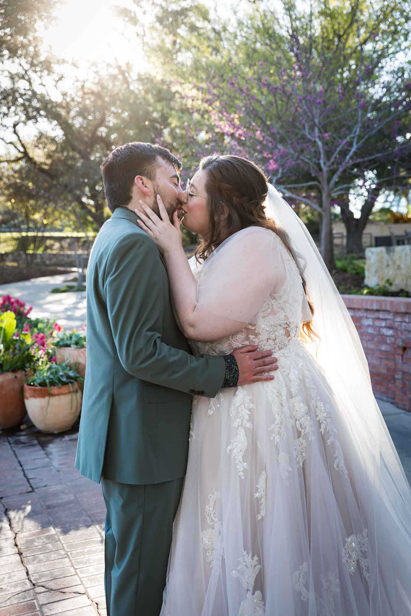 Bride kissing groom with hands on groom's face during first look before a San Antonio Botanical Garden wedding ceremony