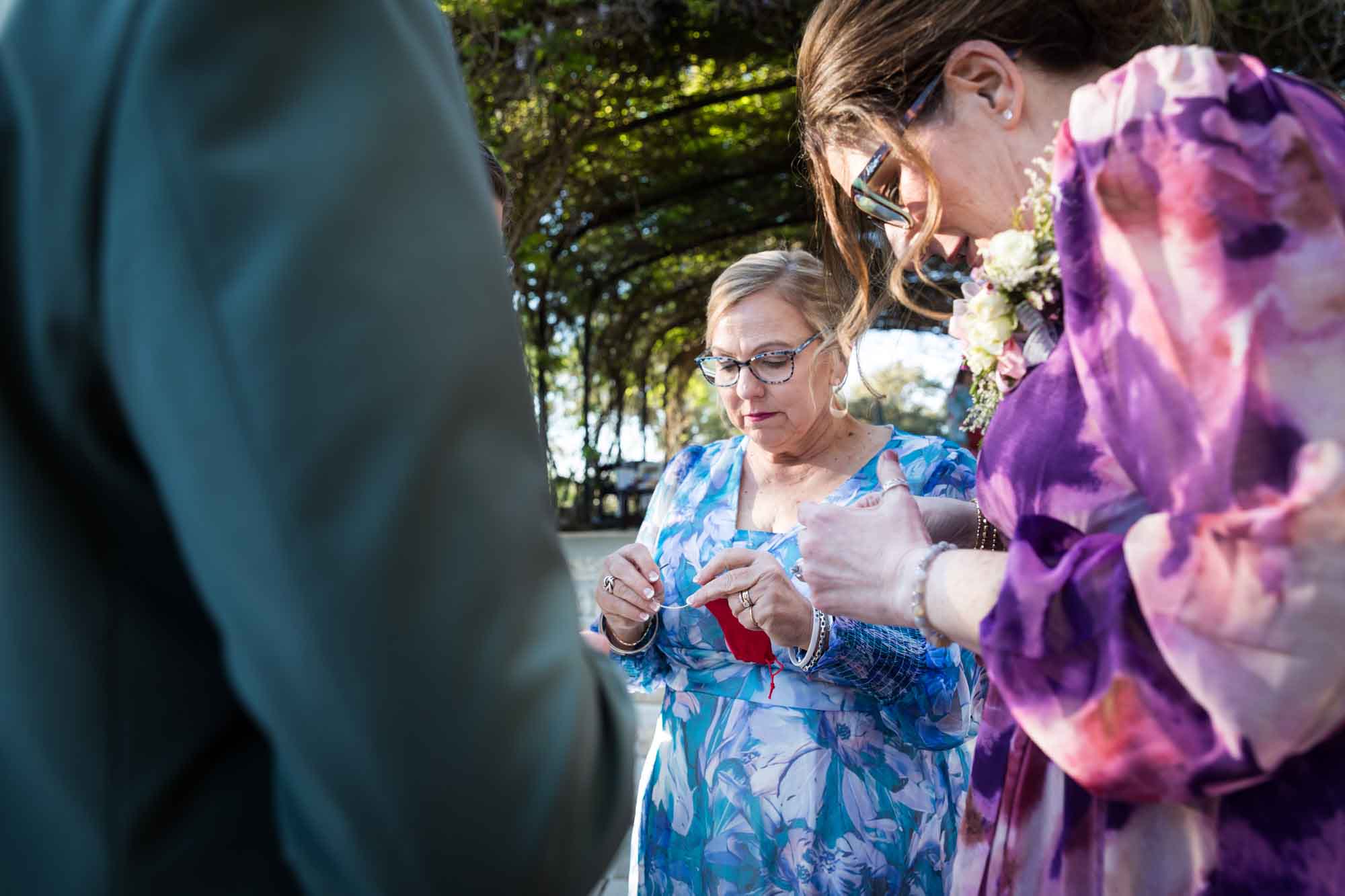 Woman wearing blue floral dress and woman wearing purple floral dress inspecting gold bracelets before a San Antonio Botanical Garden wedding ceremony