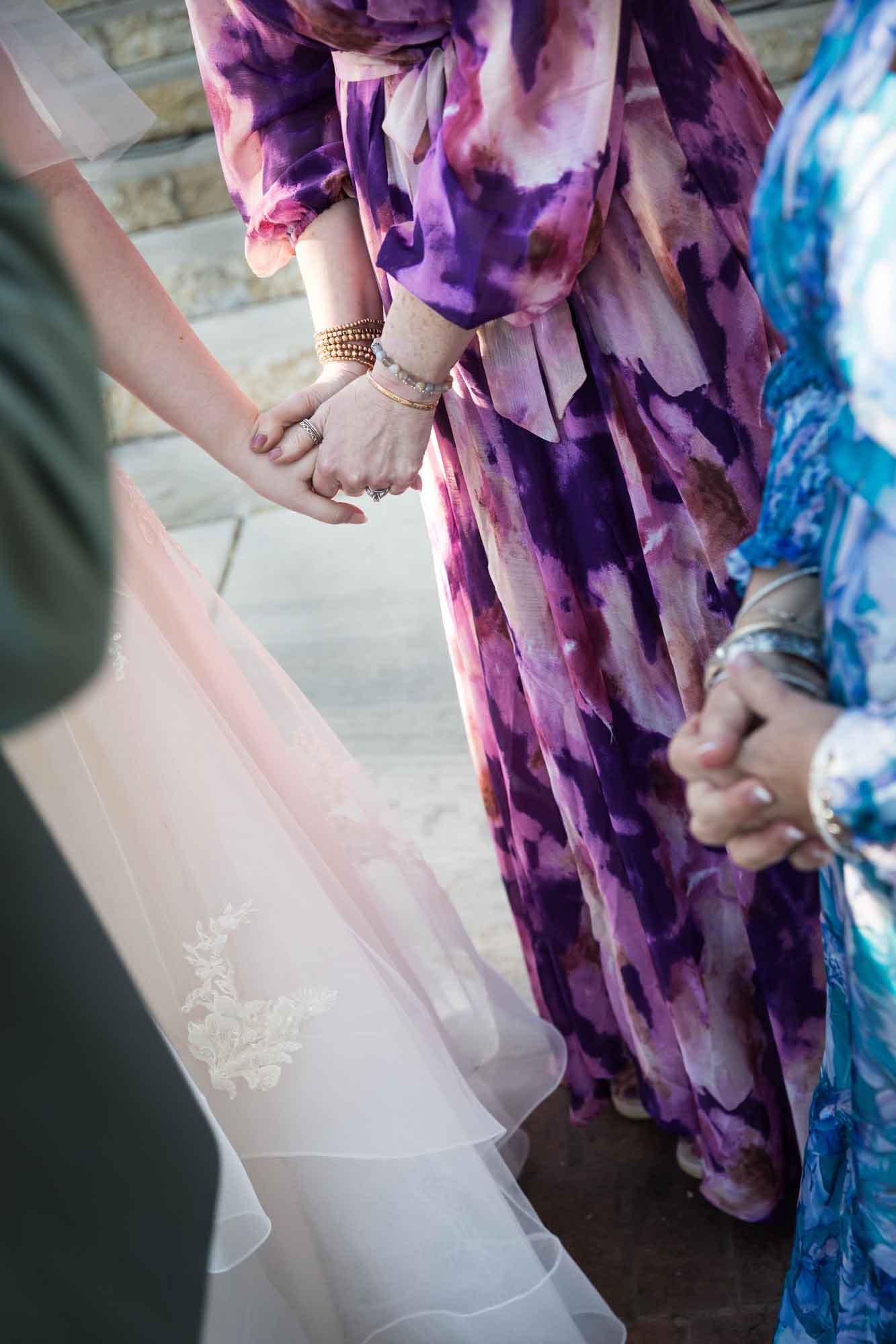 Close up of woman wearing purple floral dress holding hand of bride before a San Antonio Botanical Garden wedding ceremony