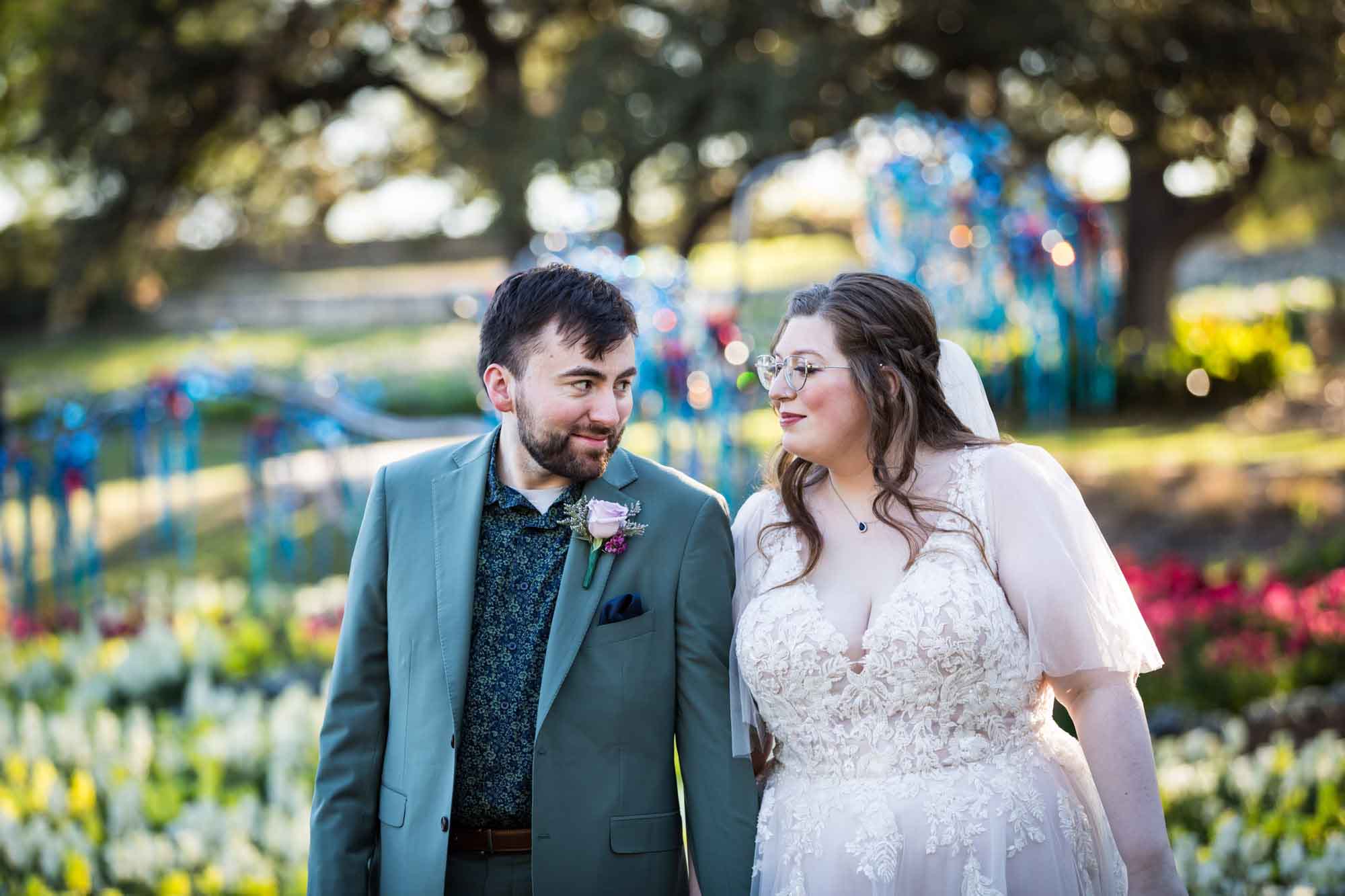 Bride and groom standing in front of bed of colorful snapdragons and trees before a San Antonio Botanical Garden wedding ceremony