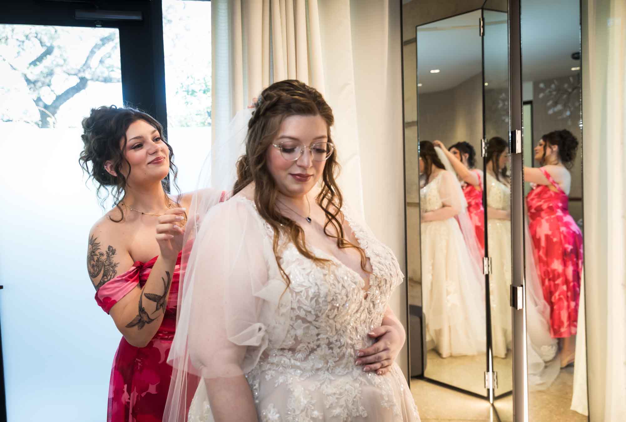 Woman wearing red floral dress adjusting bride's veil in front of mirror before a San Antonio Botanical Garden wedding ceremony