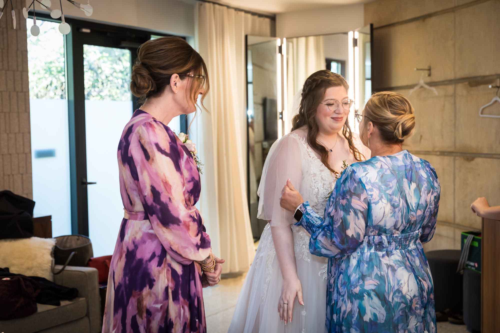 Bride talking with two older woman wearing floral dresses in bridal suite before a San Antonio Botanical Garden wedding ceremony
