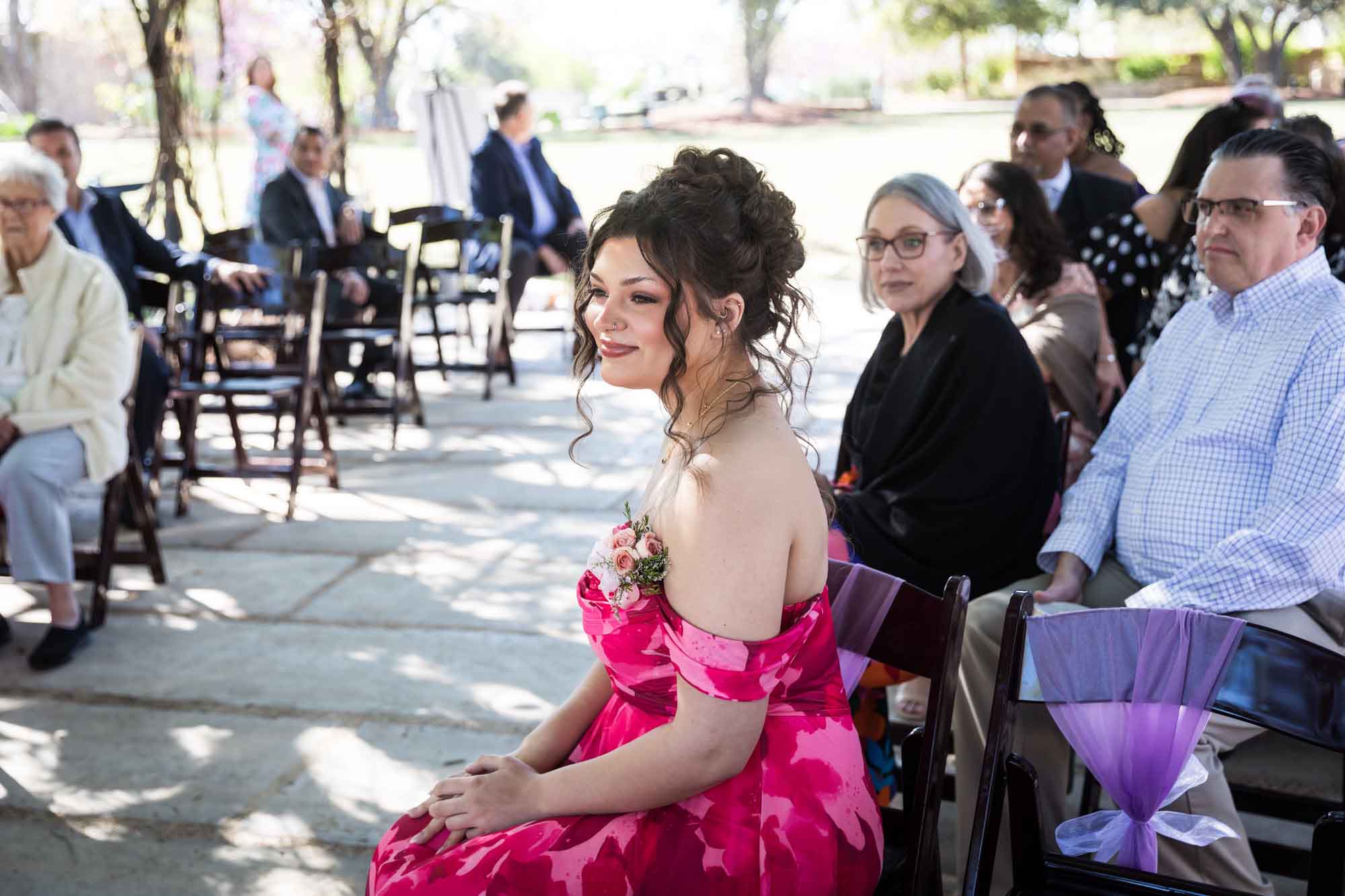Woman wearing strapless, red floral gown sitting in front of other guests during a San Antonio Botanical Garden wedding ceremony
