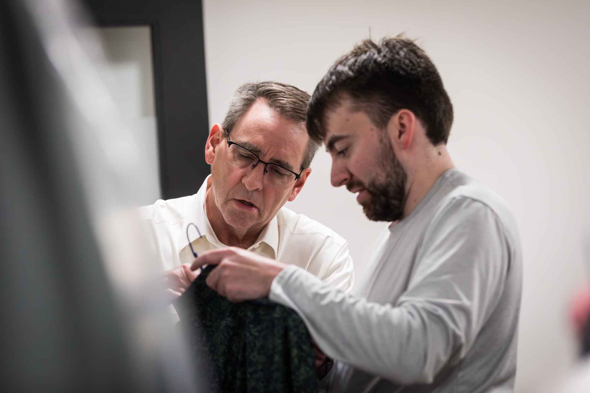 Father and son inspecting a shirt in a room before a San Antonio Botanical Garden wedding ceremony