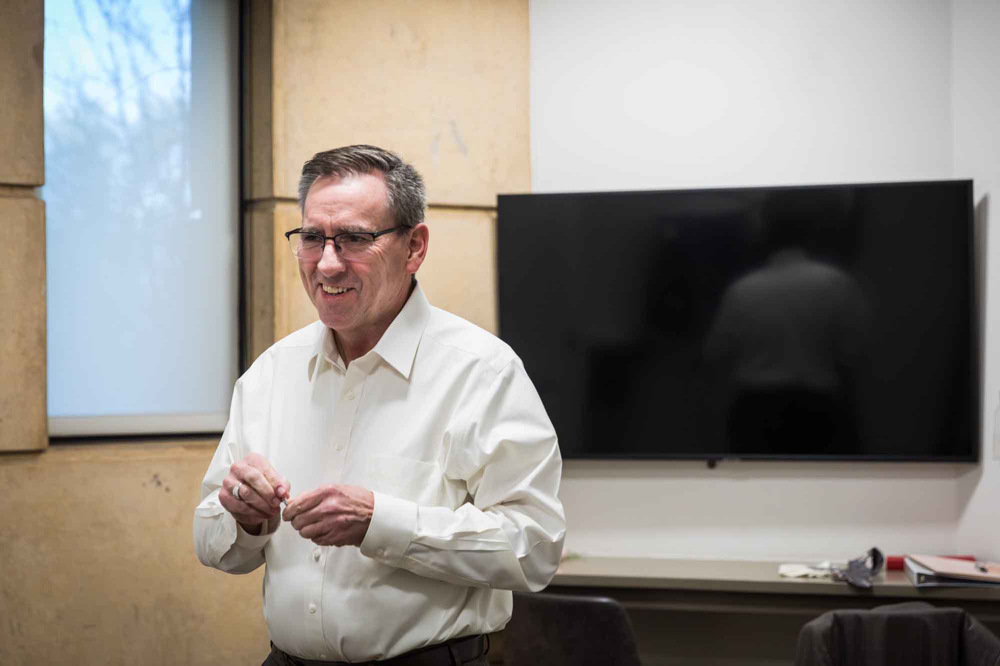 Father holding a small object in front of a TV screen in a room before a San Antonio Botanical Garden wedding ceremony