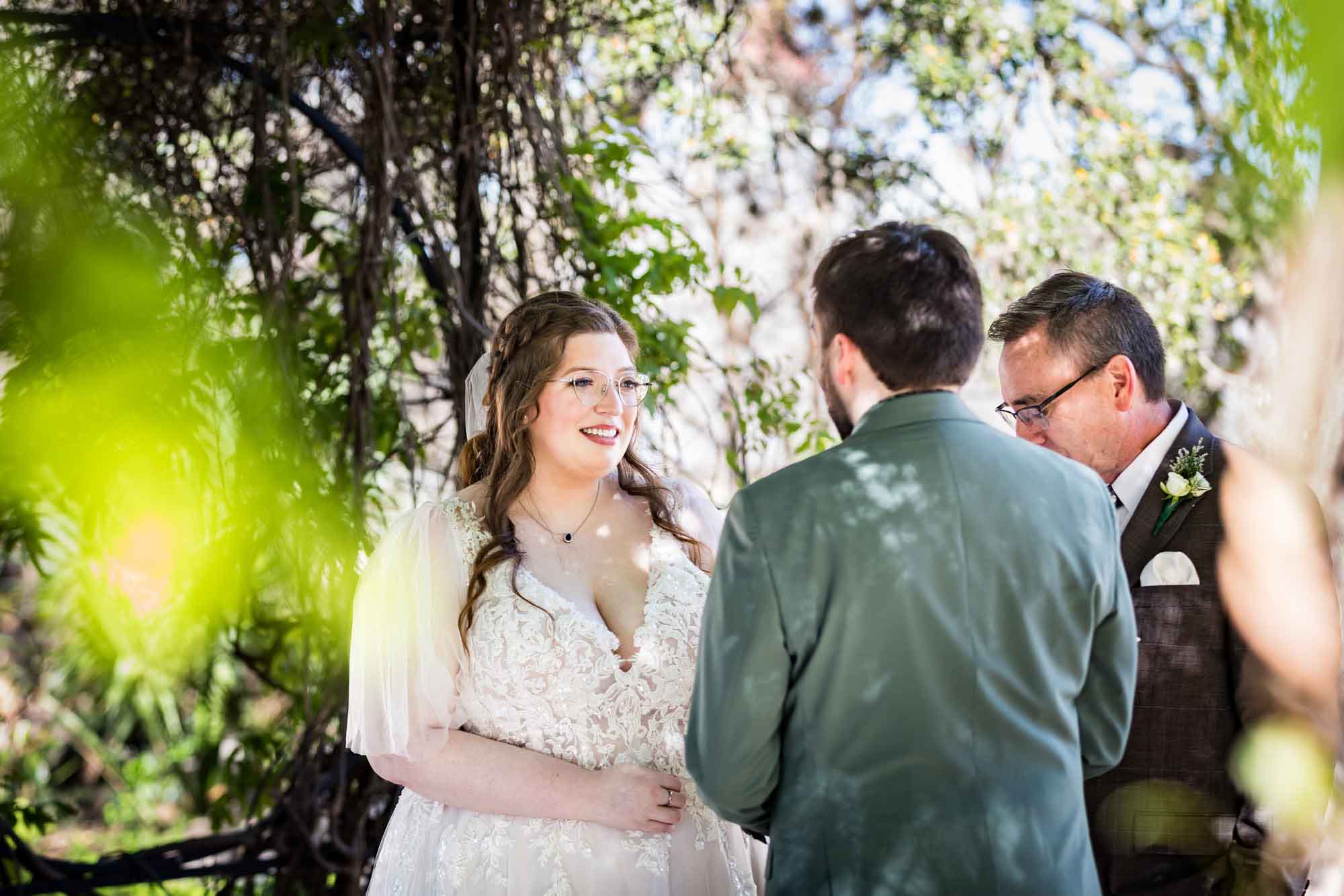 Bride listening to groom in front of officiant under Wisteria Arbor during a San Antonio Botanical Garden wedding ceremony