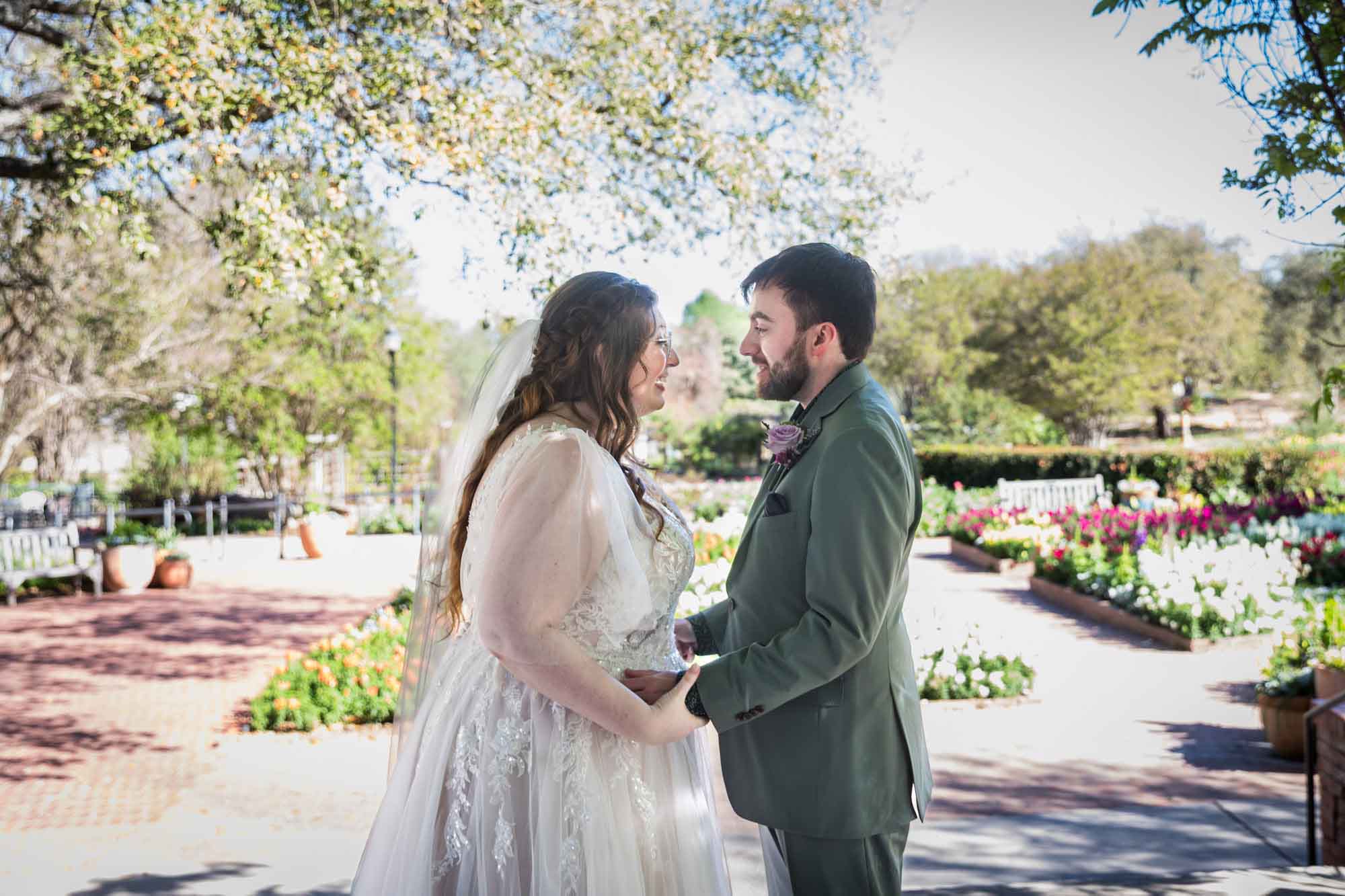 Bride and groom holding hands in front of colorful flowers during a San Antonio Botanical Garden wedding ceremony
