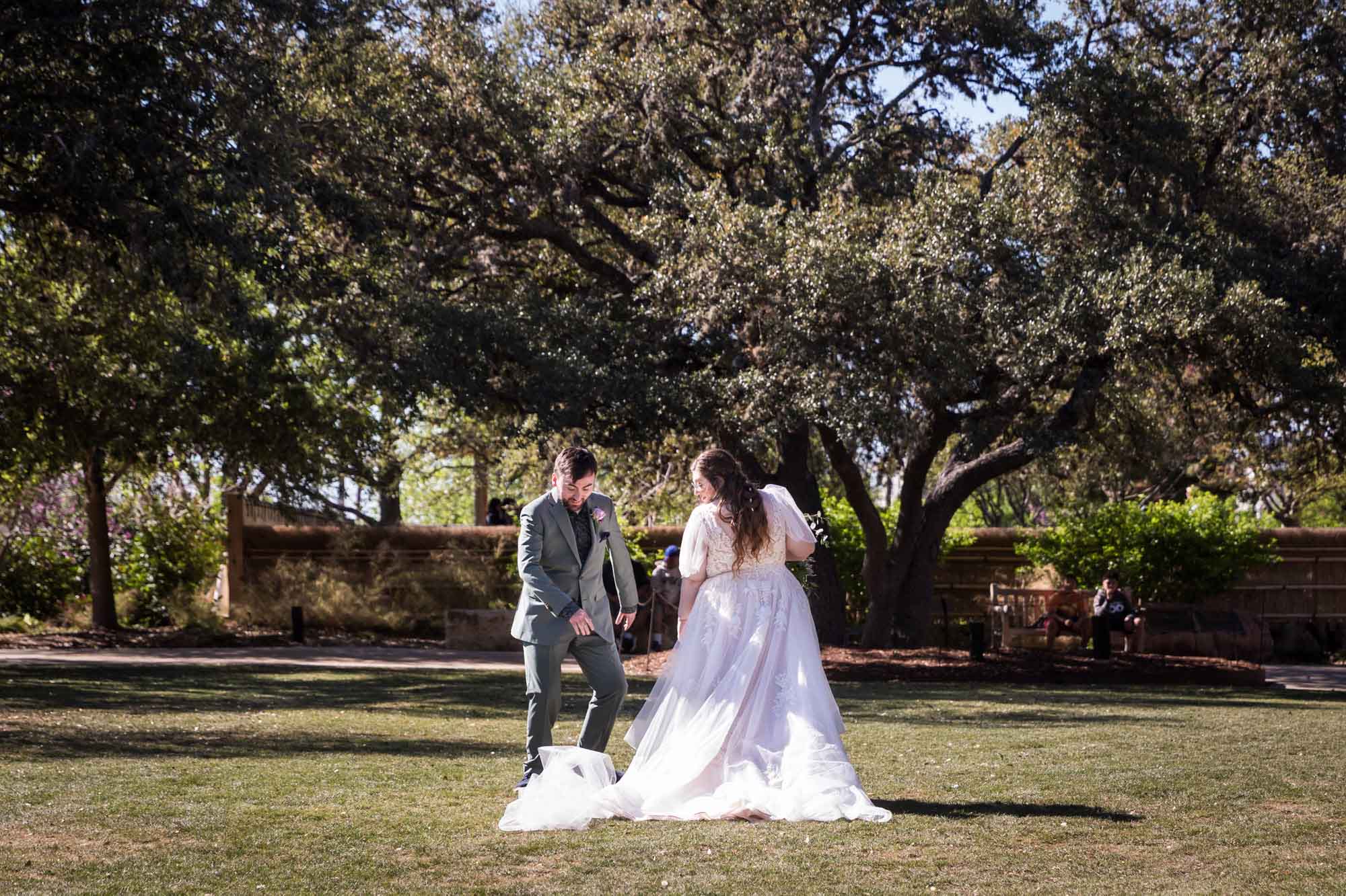 Groom looking down at veil on ground behind bride during a San Antonio Botanical Garden wedding ceremony