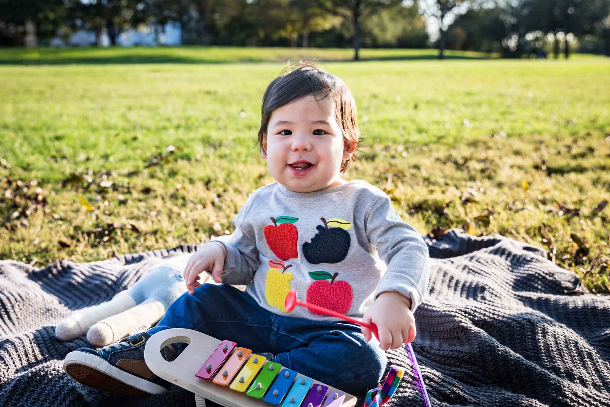 Little boy playing with toys while sitting on blanket on grass during a Mueller Lake Park family portrait