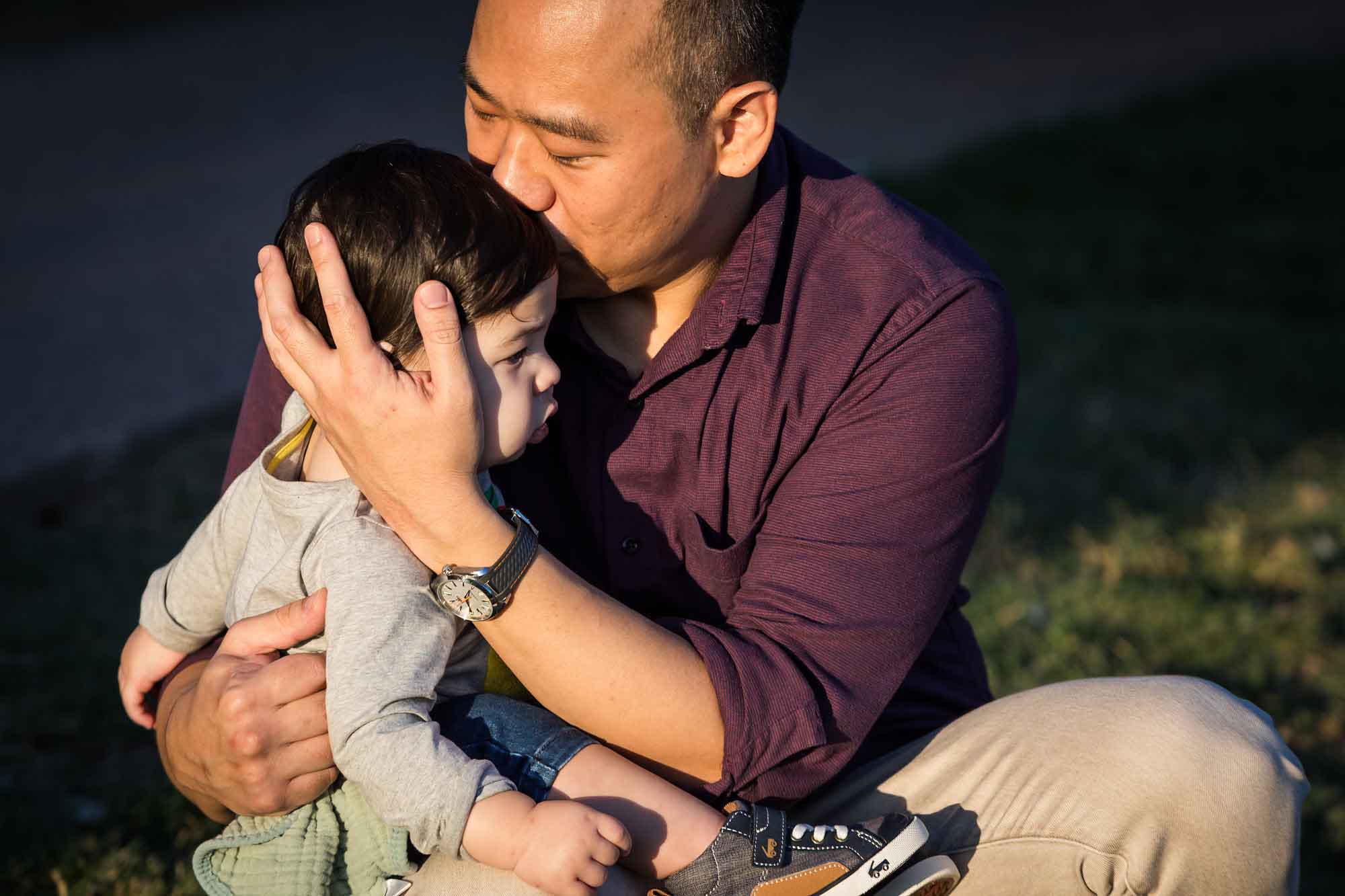 Little boy being kissed on head by father wearing purple shirt during a Mueller Lake Park family portrait