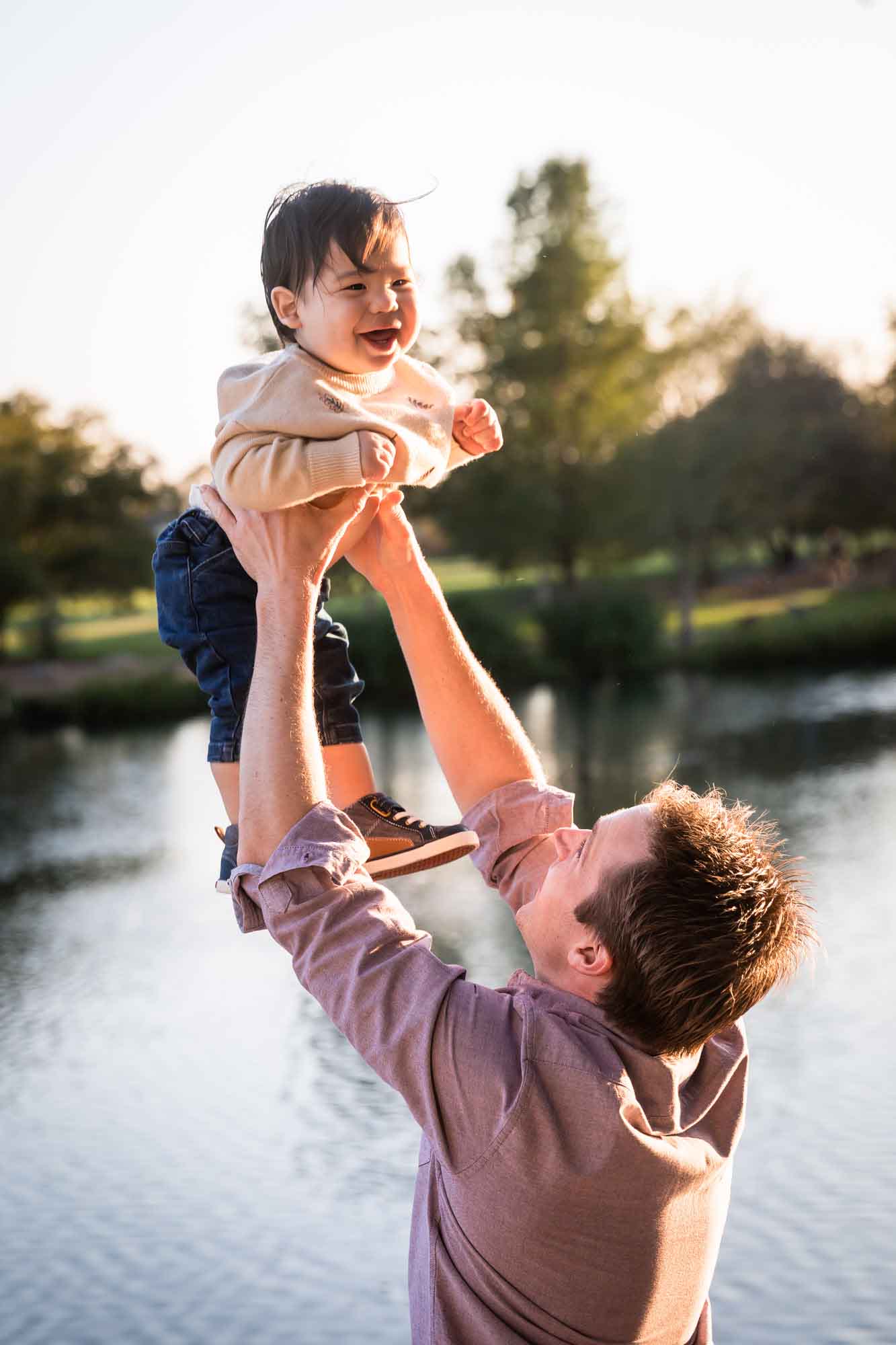 Little boy being thrown in the air by father wearing pink shirt beside Mueller Lake during a Mueller Lake Park family portrait