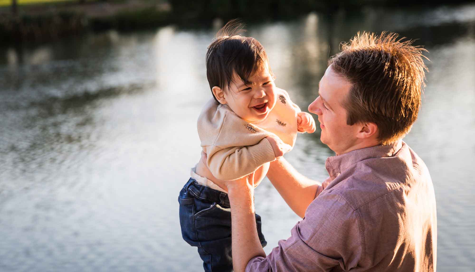 Little boy playing with father wearing pink shirt beside Mueller Lake during a Mueller Lake Park family portrait