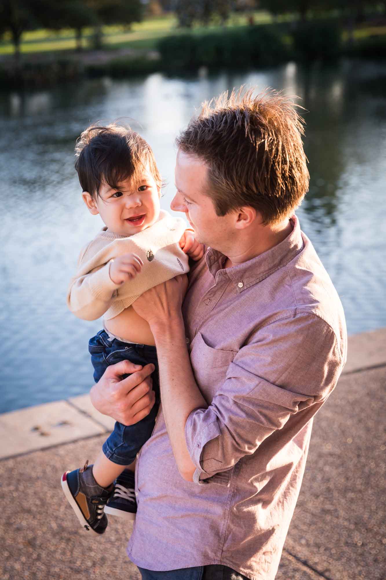 Little boy playing with father wearing pink shirt beside Mueller Lake during a Mueller Lake Park family portrait