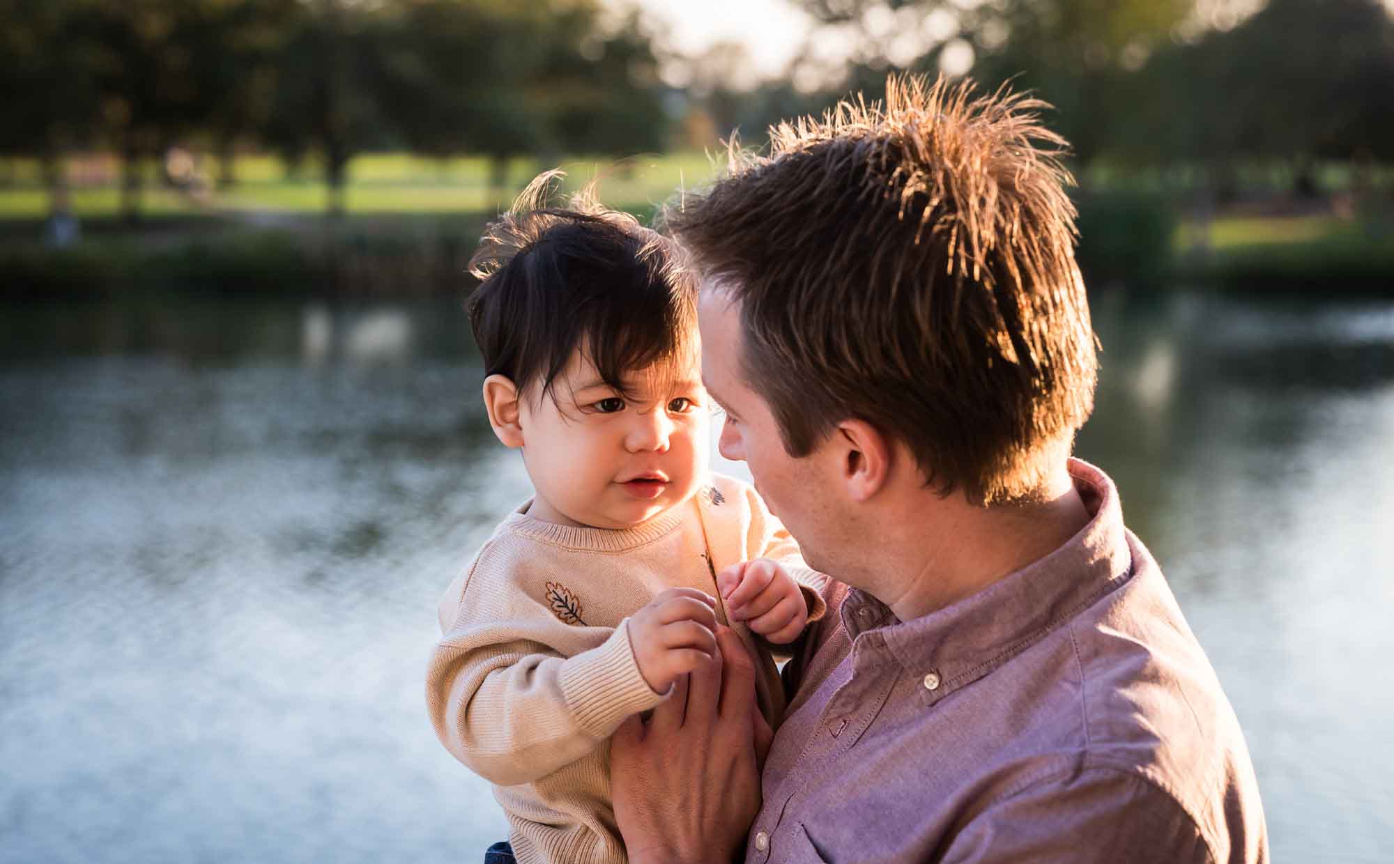 Little boy playing with father wearing pink shirt beside Mueller Lake during a Mueller Lake Park family portrait