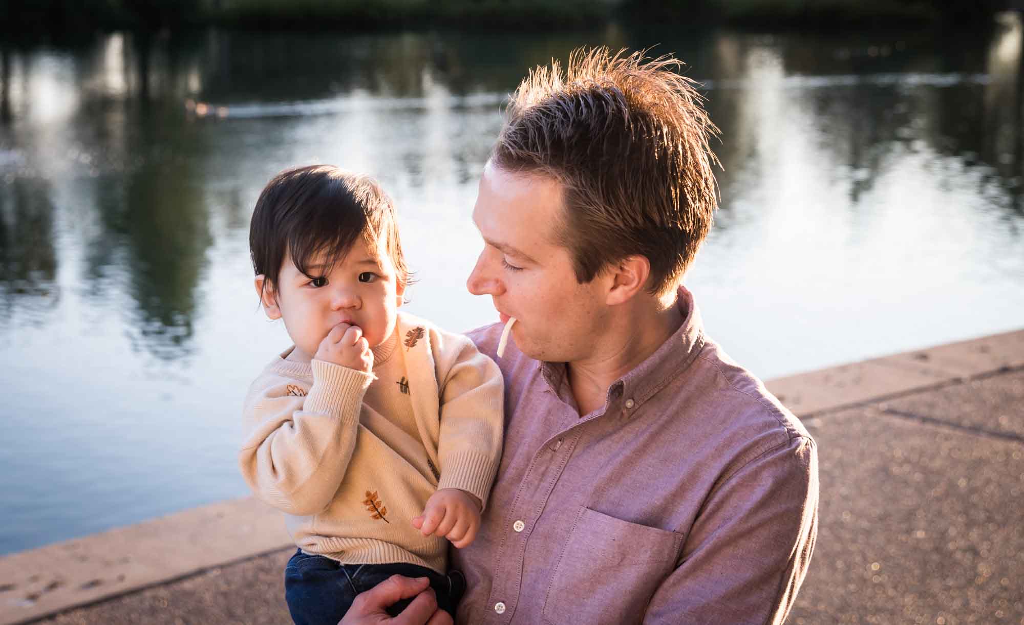 Little boy playing with father wearing pink shirt beside Mueller Lake during a Mueller Lake Park family portrait