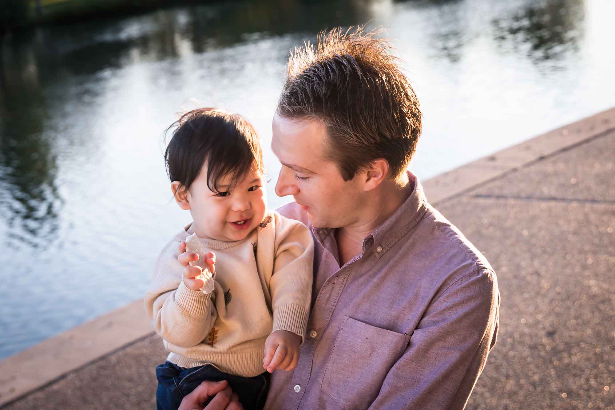 Little boy playing with father wearing pink shirt beside Mueller Lake during a Mueller Lake Park family portrait