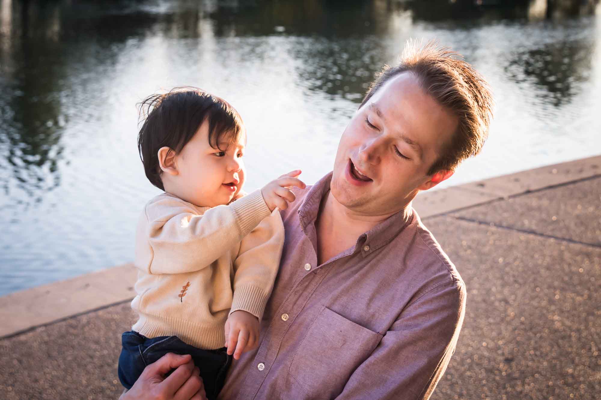 Little boy playing with father wearing pink shirt beside Mueller Lake during a Mueller Lake Park family portrait