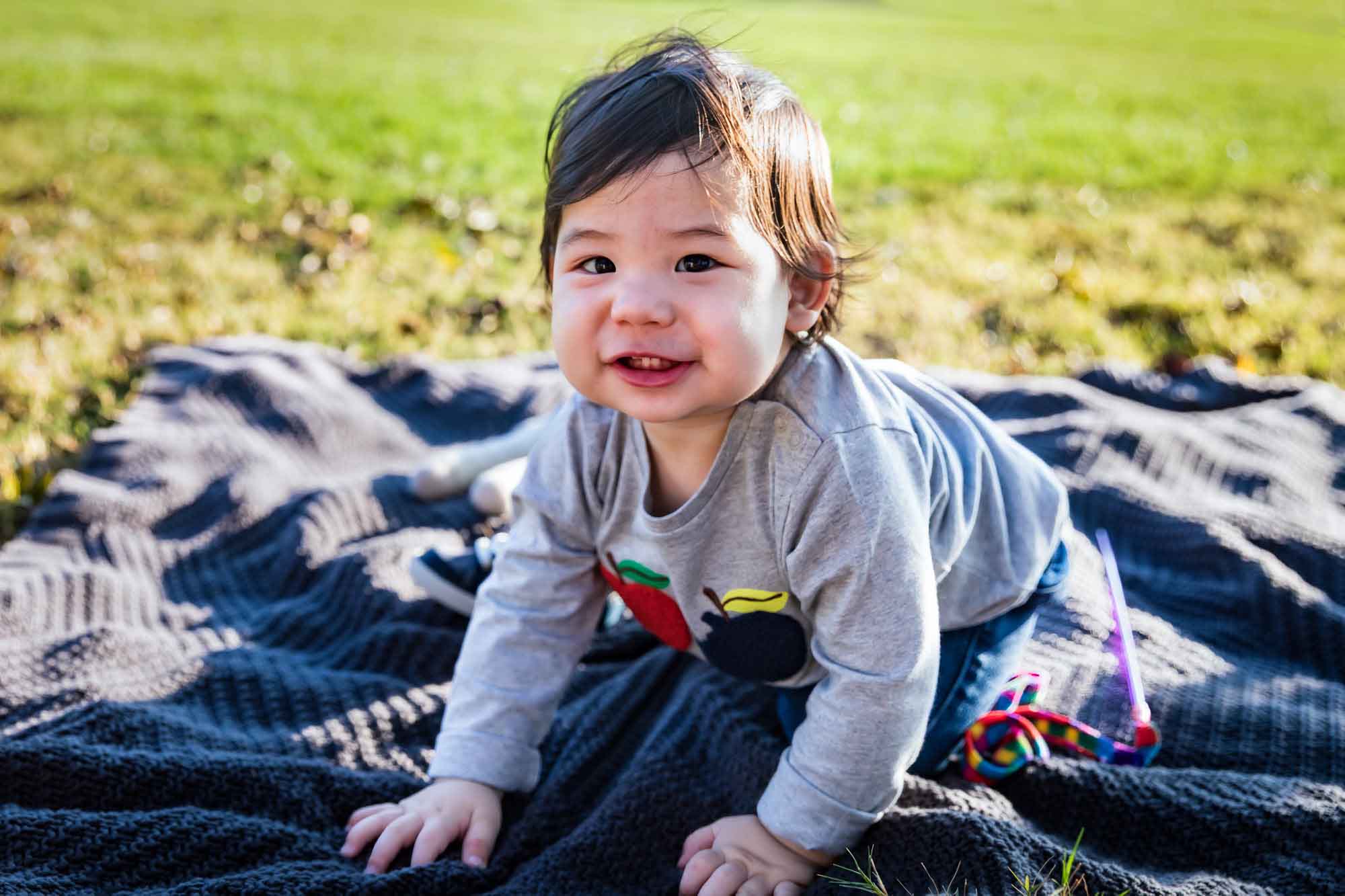Little boy playing with toys while sitting on blanket on grass during a Mueller Lake Park family portrait